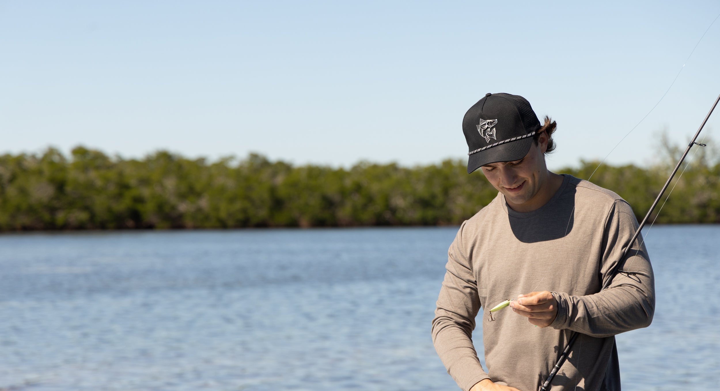 Man fishing by a body of water with trees in the background